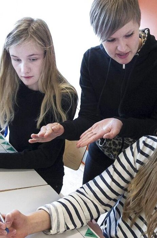 To piger får hjælp til lektier af en lærer.